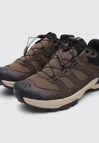 Baskets de sport brunes en mesh et matériaux synthétiques, dotées d'une semelle en caoutchouc noir robuste, d'un design sans couture et de lacets élastiques.