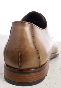 Bruine leren schoen met een gladde textuur, afgeronde achterkant, contrasterende stiksels, houten hak en zwarte accentband aan de basis.