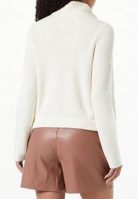 Pull encolure bénie crème à côtes avec une coupe ajustée, accompagné de shorts marron en simili cuir taille haute, présentant une texture lisse et un design soigné.