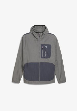 Lichte grijze jas met capuchon, voorzien van een donkerblauwe accentzak en rits, met een soepele textuur en een sportief ontwerp.