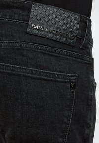 Κοντινή λήψη τσέπης μαύρων τζιν denim με υφασμάτινη μαύρη δερμάτινη ετικέτα που γράφει KARL LAGERFELD πάνω από την τσέπη.