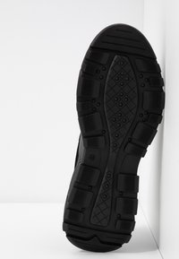 Semelle extérieure de chaussure de sport noire en caoutchouc texturé, présentant une surface antidérapante à motifs et des zones en relief pour l'adhérence et la durabilité.