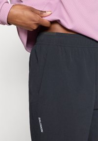 Μαύρο αθλητικό παντελόνι με ελαστική μέση, με πλαϊνές τσέπες και μικρό λευκό λογότυπο. Το υλικό φαίνεται ελαφρύ και λείο.