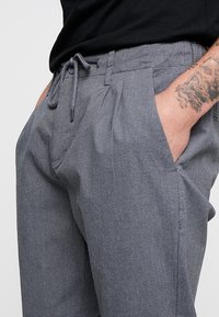 Pantaloni grigi in tessuto intrecciato con vita regolabile, fit rilassato etasche laterali, caratterizzati da un leggero motivo testurizzato.