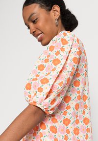 Vestido floral com mangas bufantes, feito de tecido leve, com uma base branca e flores multicolores em laranja, rosa e verde.