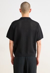 Black short-sleeve knit top featuring a textured design with open weave, ribbed collar, and hem. Suitable for layering or standalone wear.