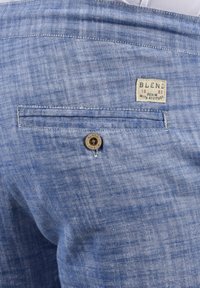 Lyseblå denim-bukser med en glatt tekstur. Har en baklomme med knapp og et vevet merke med teksten "BLEND" og "DENIM 93."