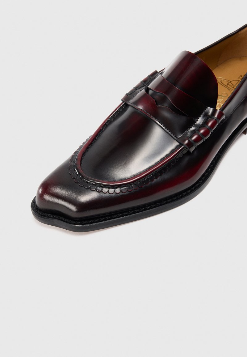 Mocassin en cuir bordeaux pour homme avec un bout pointu, une bande texturée, des coutures décoratives et une finition lisse. Semelle en caoutchouc pour une meilleure traction.