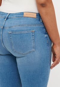 Blue denim jeans featuring a close-fitting design, five pockets, and a leather waistband label. The texture is smooth with a slight stretch.