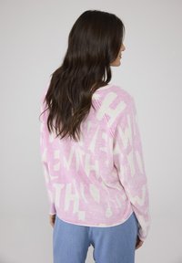 Hellrosa Pullover mit weißem abstraktem Textmuster. Lange Ärmel, runder Ausschnitt, weiche Textur und lockere Passform.