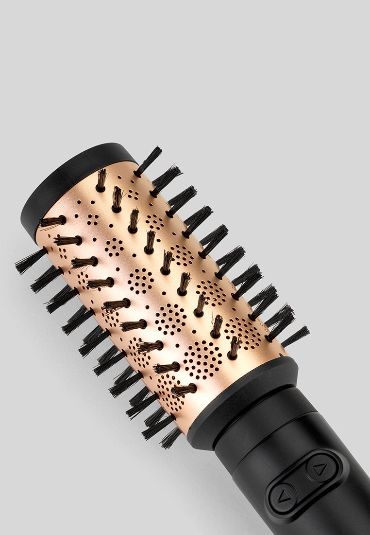 Brosse à cheveux ronde avec un corps métallique en rose doré, dotée de poils noirs et de trous de ventilation, combinée à une prise noire et des boutons de contrôle.