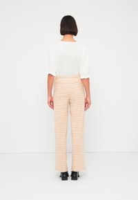 Λευκό τοπ με φουσκωτά μανίκια και cropped τελείωμα, συνδυασμένο με ριγέ παντελόνι σε ροδακινί και λευκό. Μαύρα μπότες με τακούνι ολοκληρώνουν την εμφάνιση.