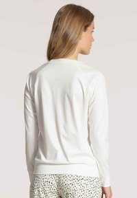 White long-sleeve top with a round neckline and ribbed cuffs, featuring a smooth texture and a relaxed fit. Accented with raglan sleeves.