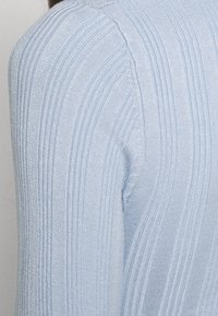 Pull tricoté bleu clair avec texture à côtes verticales, coupe ajustée et manches longues, vu de l'épaule et du haut du dos.
