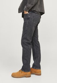 Jeans de mezclilla oscura con corte recto, con costuras claras y cinco bolsillos, complementados con botas de trabajo marrones.