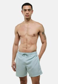 Shorts de bain rayés en vert clair et blanc, fabriqués en tissu léger. Ils disposent d'une taille élastique avec un cordon de serrage pour un ajustement parfait.