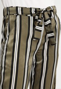 Pantalones a rayas en verde oliva, negro y blanco, con un acabado satinado, cinturilla con hebilla y bolsillos laterales para mayor funcionalidad.