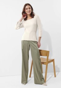 Cremfarbener gerippter Pullover mit quadratischem Ausschnitt und Dreiviertelärmeln, kombiniert mit olivgrünen weit geschnittenen Hosen und beigen spitzen Absätzen.