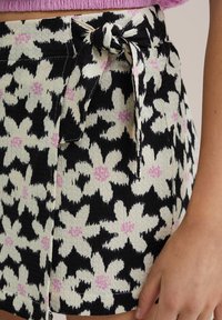 Black and white floral print skirt with pink accents, featuring a textured fabric and a tied waistband detail.