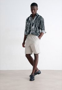 Zwart-wit gestreepte shirt, lichtbeige shorts en zwarte instappers. Het shirt heeft lange mouwen en een relaxte pasvorm.