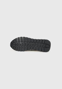 Svart gummisåle til sneakers med dype spor, teksturerte mønstre, og "KARL LAGERFELD" preget i sentrum.