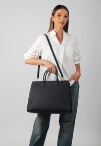 Black leather tote bag with a structured design, dual handles, and a detachable shoulder strap. Features gold-tone hardware and textured surface.