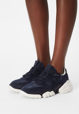 Navyblauwe sneakers van mesh en suède materialen, met een dikke witte zool en drie bandjes voor een stevige pasvorm.