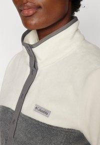 Kraagloze fleece trui in crème en grijs. Beschikt over een knopenlijst en een Columbia-logo patch. Zachte textuur met een kleur-blokontwerp.