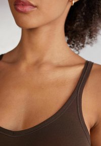 Brun linne i mjukt tyg med tunna axelband och rundad halsringning, som framhäver en åtsittande design och platta sömmar.