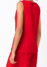 Top rosso senza maniche in cotone, con scollatura rotonda e vestibilità rilassata. Texture liscia con cuciture nette e senza decorazioni visibili.