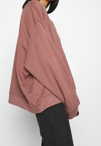 Sweat-shirt oversize de couleur rose doux, fabriqué en tissu doux avec une texture brossée. Il présente des manches dolman et un ourlet côtelé.