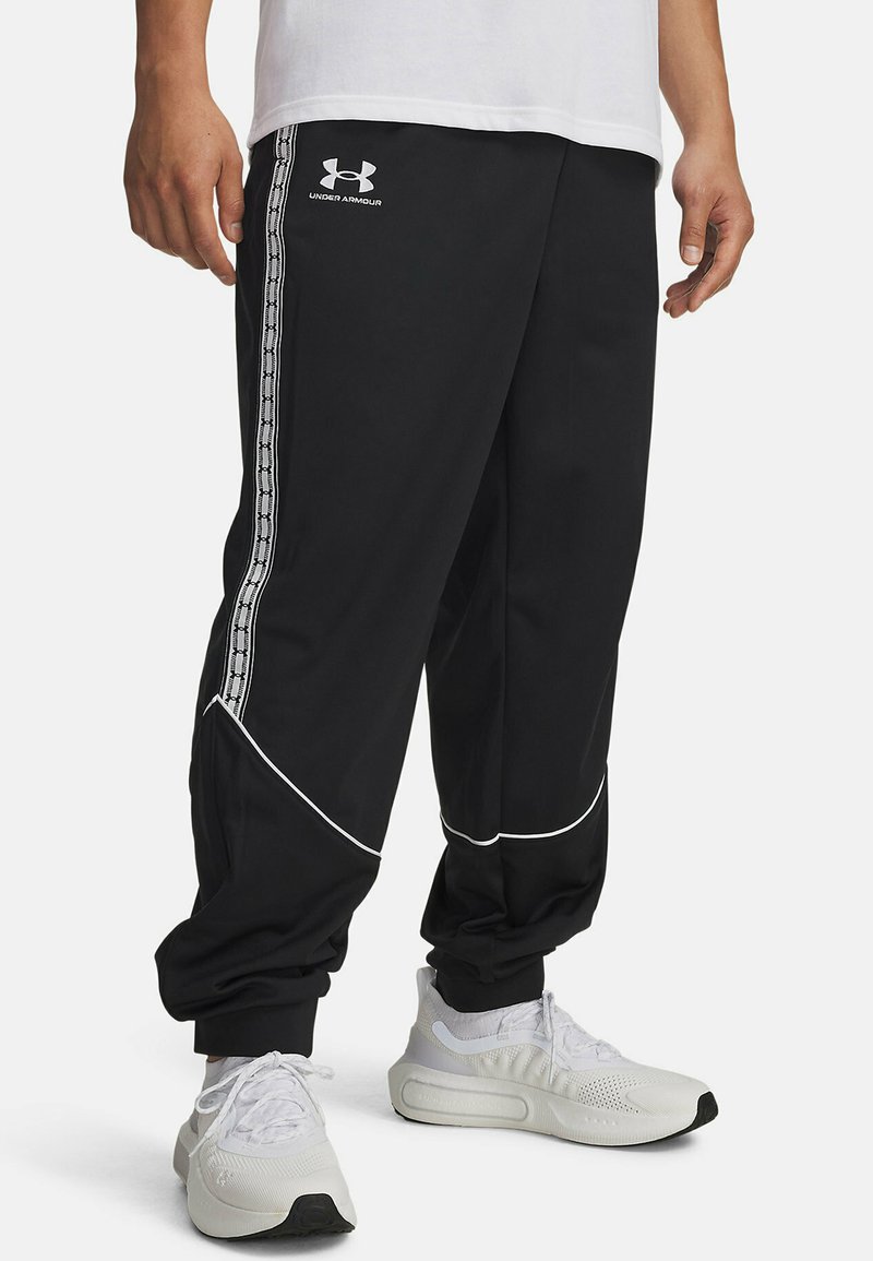 Black track pants made of smooth fabric, featuring white piping and side stripes with a logo. Tapered fit with elastic cuffs at the ankles.