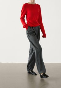 Pull en tricot rouge à manches longues, associé à un pantalon gris taille haute, bien ajusté ; présentant des jambes droites et des mocassins noirs.