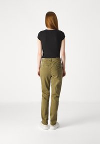 Alyvuogių žaliai kelnės, pagamintos iš medvilnės mišinio, su tiesiomis kojomis ir užpakalinėmis kišenėmis, derinamos su juodu prigludusiu marškinėliu.