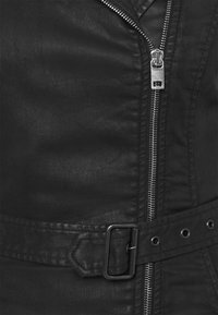 Veste noire en simili cuir avec une fermeture éclair argentée, une ceinture à boucle rectangulaire et des coutures décoratives le long des coutures.