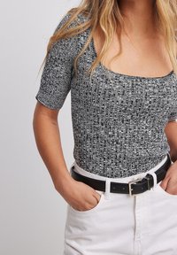 Top aderente a maniche corte con motivo bianco e nero, abbinato a pantaloni bianchi a vita alta e una cintura nera.