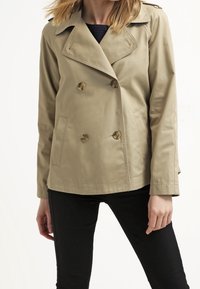 Beige dubbelknäppt trench coat med stora runda knappar, skräddarsydd krage, två sidofickor och en slät textur.