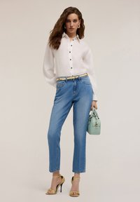 Camicia bianca con bottoni e maniche lunghe, jeans blu a gamba dritta, sandali gialli con tacco alto e una piccola borsa verde mentolato.