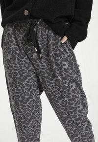 Grå joggerbukser med et sort dyreprintmønster, justerbar snor i taljen og sidelommer, parret med en sort striktrøje.