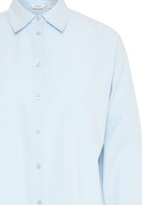 Camisa abotonada de color azul claro con un cuello clásico, fabricada en suave algodón, de manga larga y con un ligero brillo, que presenta botones transparentes en el frente.