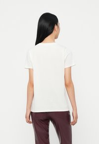 Camiseta blanca de algodón con cuello redondo, mangas cortas y corte recto, combinada con pantalones burdeos oscuros. Diseño sencillo, sin patrones visibles.