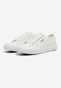 Sneakers bianchi in tela con punta arrotondata, cinque fori per i lacci, suola in gomma e un piccolo logo sul lato. Il tessuto ha una texture liscia.