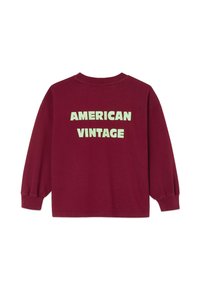 Sweat-shirt bordeaux à manches longues, coupe ample, col côtelé, et grand texte vert clair indiquant « AMERICAN VINTAGE » au dos. Matière en coton.