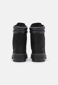 Botas negras hasta el tobillo con acabado de ante, collar de cuero acolchado y suela de goma texturizada. Presenta una marca en el lateral.