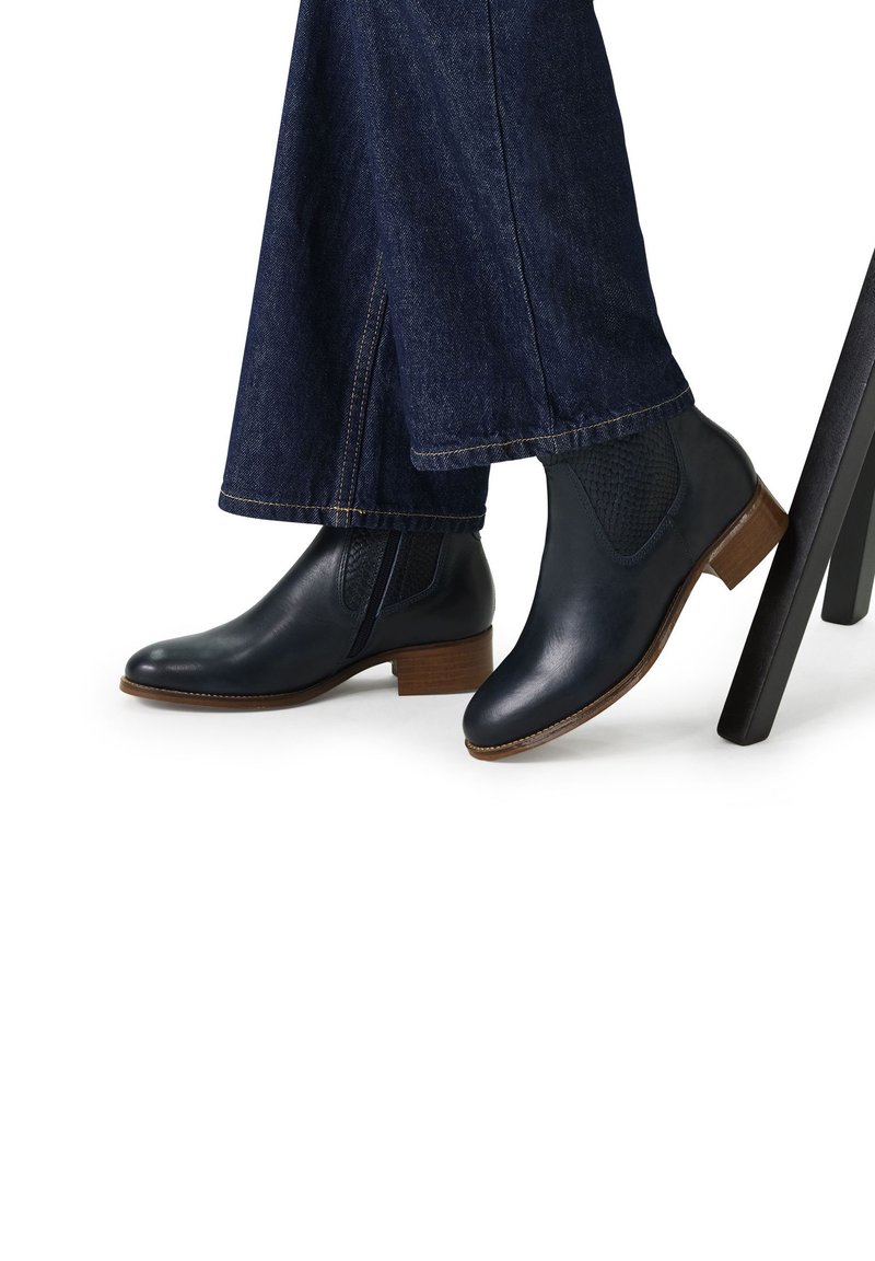Dunkelblaue Leder-Ankle-Boots mit elastischen Seiteneinsätzen, Holzblock-Absätzen und glatter Oberfläche, getragen mit weit geschnittenen Jeans.