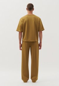 Korte mouwen, mosterdkleurige top gecombineerd met bijpassende loszittende broek. Glad materiaal, minimalistisch ontwerp en een ontspannen silhouet.