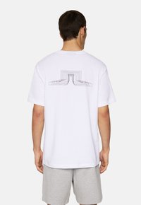 Vit bomullströja med en geometrisk svart linjegrafik tryckt på baksidan, med rund hals och korta ärmar.