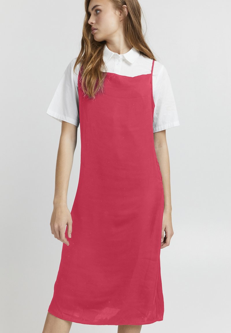 Abito senza maniche rosa realizzato in tessuto morbido, con un taglio dritto, abbinato a una camicia bianca con colletto sotto.