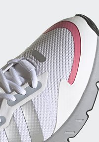 Zapatilla blanca con parte superior de malla texturizada, acentos grises, detalles en rosa y suela de goma estampada. Presenta cordones y elementos reflectantes.
