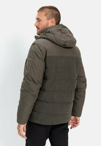 Polstret jakke i dyb grøn med en struktureret overflade, hætte og en sidelomme. Har vandrette quiltede sektioner og kontrasterende panel.